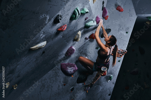 Young woman in shorts and sports bra exercising on a bouldering wall indoors.