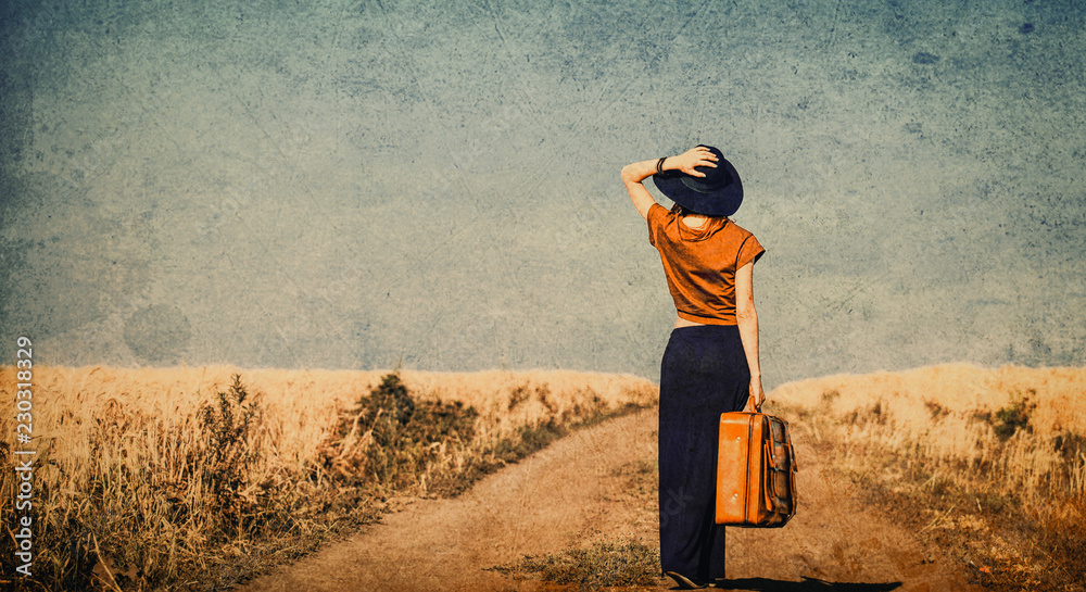 Fototapeta premium photo of the beautiful young woman with suitcase on the countryside road
