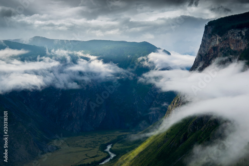 From the height of the green river valley in the mountains at the height of the clouds in the morning. A mountain pass in the Altai Republic at sunrise. River and green meadows from height of flight