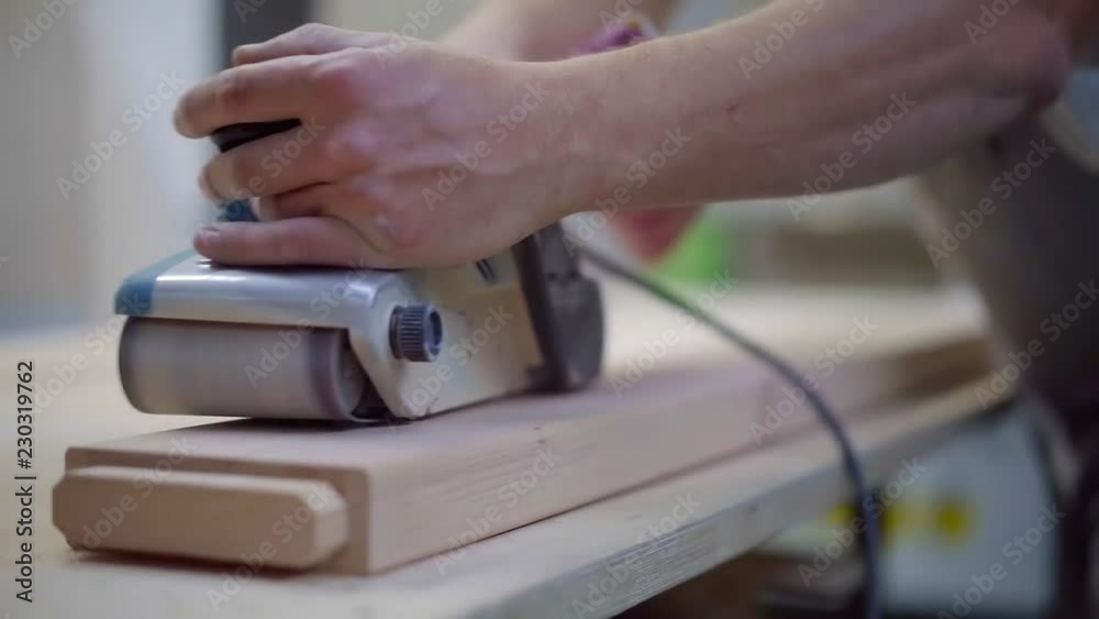 master is sanding wooden beam by polishing machine, moving it by hands, close-up in workshop master is sanding wooden beam by polishing machine, moving it by hands, close-up in workshop