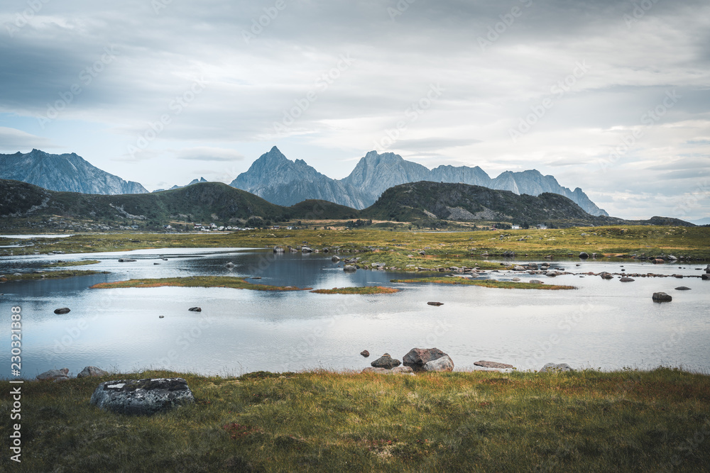 The magical reflections of the mountains in the clear water on y cloudy day. Water with grass in the foreground, mountains in the background. During the summer trip to the Norwegian north. Lofoten