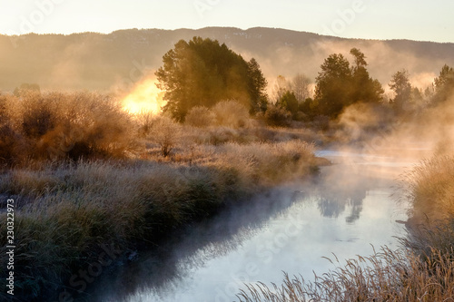 Morning sun burning through the fog above a mountain stream