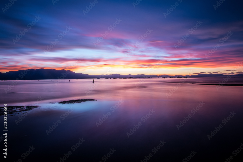 Beautiful sunset on Lake Tahoe with bright purple, pinks and oranges in the sky. Long exposure, calm water