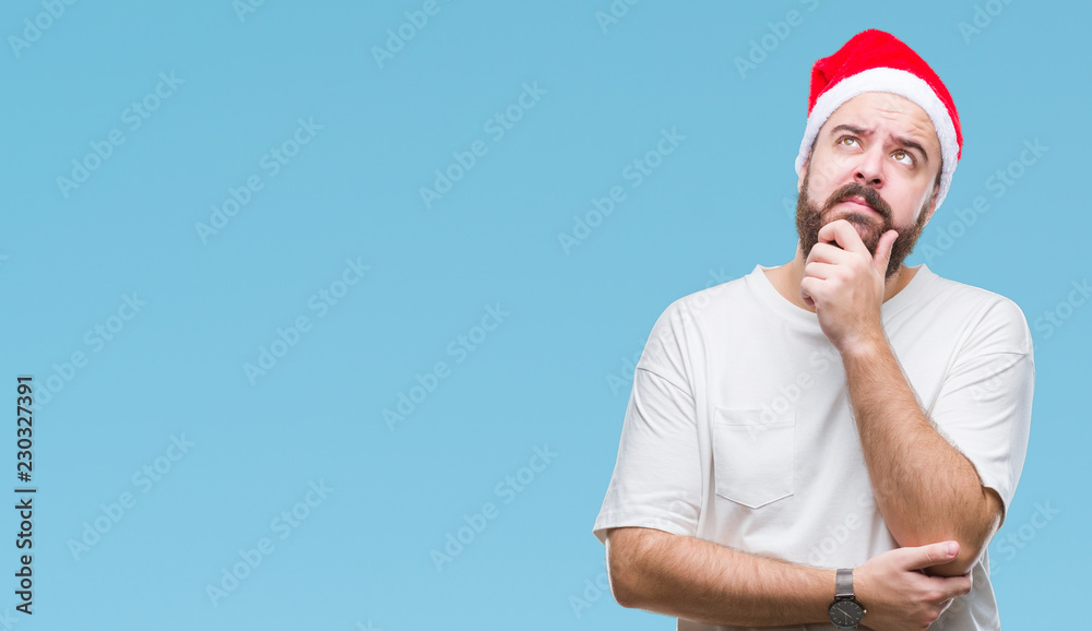 Young caucasian hipster man wearing christmas hat over isolated background with hand on chin thinking about question, pensive expression. Smiling with thoughtful face. Doubt concept. Young caucasian hipster man wearing christmas hat over isolated background with hand on chin thinking about question, pensive expression. Smiling with thoughtful face. Doubt concept.
