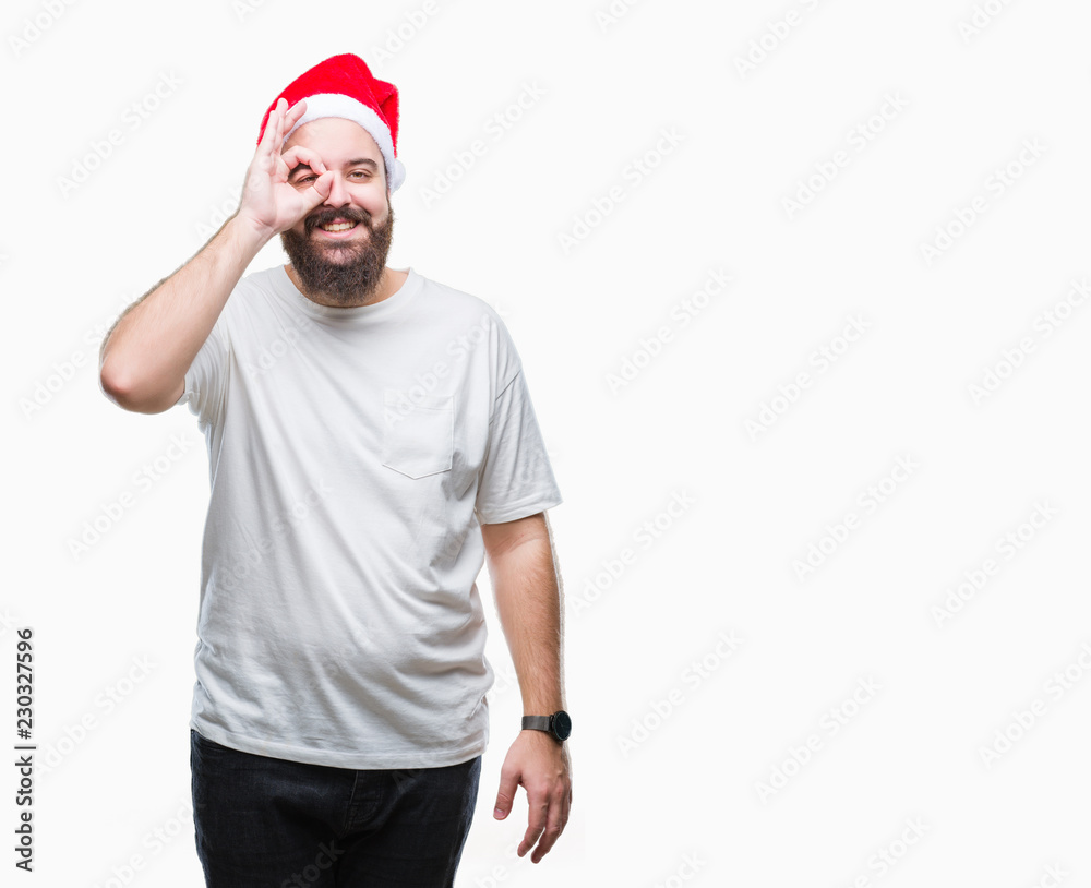 Fototapeta premium Young caucasian hipster man wearing christmas hat over isolated background doing ok gesture with hand smiling, eye looking through fingers with happy face.