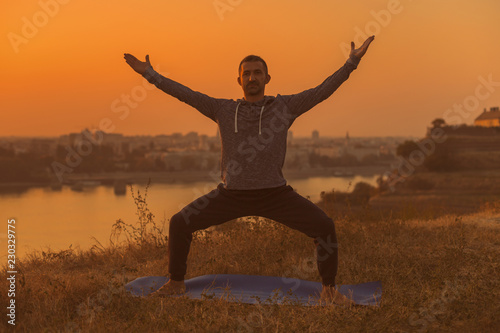 Man doing yoga on sunset with city view, Goddess Pose/Utkata Konasana.