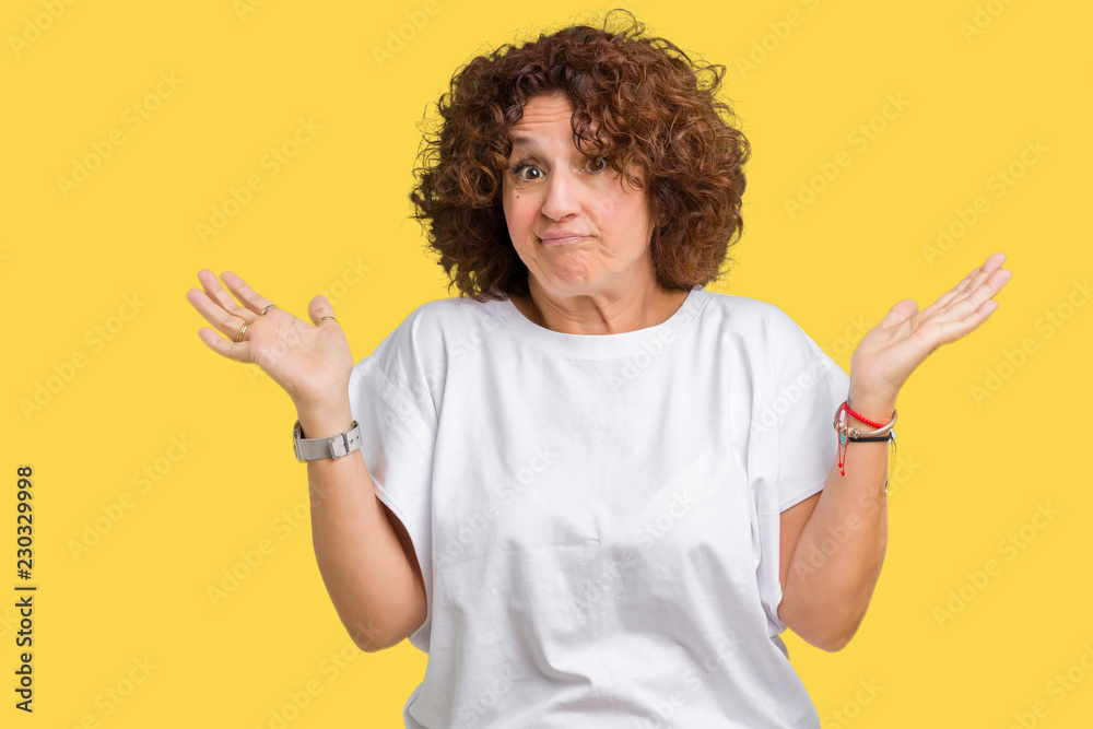 Beautiful middle ager senior woman wearing white t-shirt over isolated background clueless and confused expression with arms and hands raised. Doubt concept. Beautiful middle ager senior woman wearing white t-shirt over isolated background clueless and confused expression with arms and hands raised. Doubt concept.