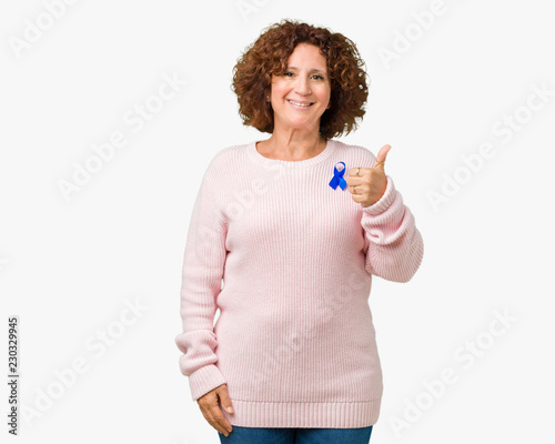 Middle ager senior woman wearing changeable blue color ribbon awareness over isolated background doing happy thumbs up gesture with hand. Approving expression looking at the camera 