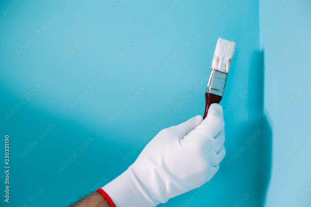 Image of man holding paintbrush in front of blue wall. Image of man holding paintbrush in front of blue wall.