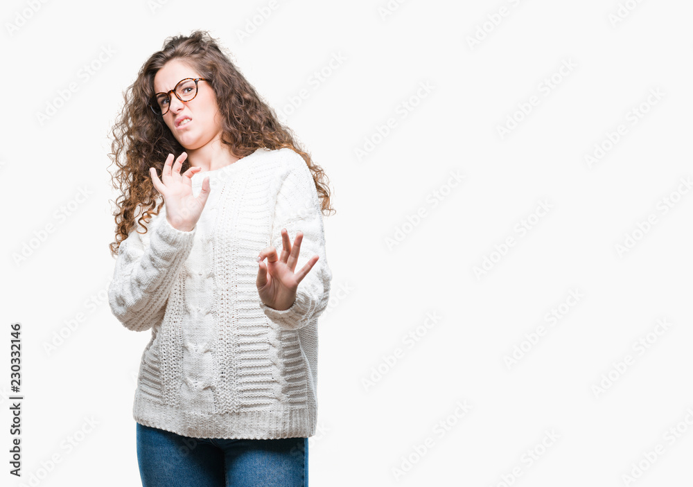 Beautiful brunette curly hair young girl wearing winter sweater over isolated background disgusted expression, displeased and fearful doing disgust face because aversion reaction. With hands raised Beautiful brunette curly hair young girl wearing winter sweater over isolated background disgusted expression, displeased and fearful doing disgust face because aversion reaction. With hands raised