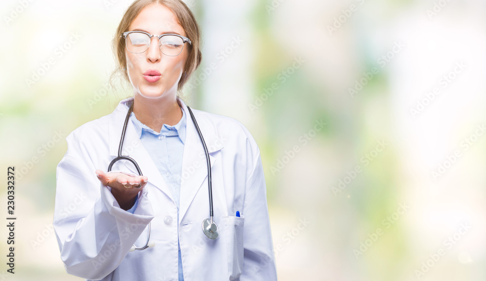 Beautiful young blonde doctor woman wearing medical uniform over isolated background looking at the camera blowing a kiss with hand on air being lovely and sexy. Love expression. Beautiful young blonde doctor woman wearing medical uniform over isolated background looking at the camera blowing a kiss with hand on air being lovely and sexy. Love expression.