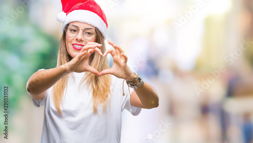 Young beautiful woman wearing christmas hat over isolated background smiling in love showing heart symbol and shape with hands. Romantic concept.