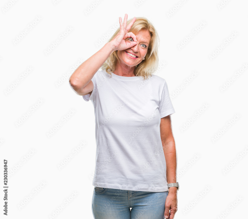 Middle age blonde woman over isolated background doing ok gesture with hand smiling, eye looking through fingers with happy face. Middle age blonde woman over isolated background doing ok gesture with hand smiling, eye looking through fingers with happy face.