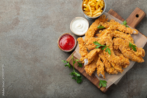 Obraz na plátně Breaded chicken strips with two kinds of sauces and fried potatoes on a wooden Board