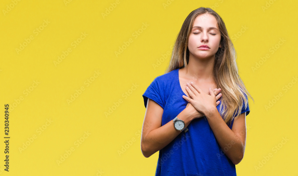 Obraz premium Young beautiful blonde woman over isolated background smiling with hands on chest with closed eyes and grateful gesture on face. Health concept.