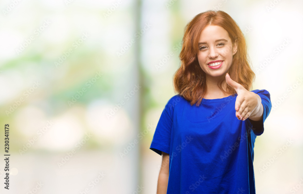 Young beautiful woman over isolated background smiling friendly offering handshake as greeting and welcoming. Successful business.