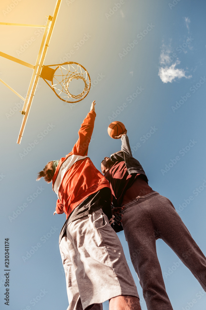 Hard game. Low angle of young well built men standing under the basketball basket while throwing the ball