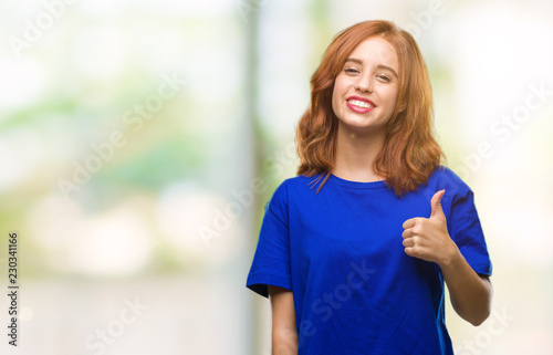 Young beautiful woman over isolated background doing happy thumbs up gesture with hand. Approving expression looking at the camera with showing success.