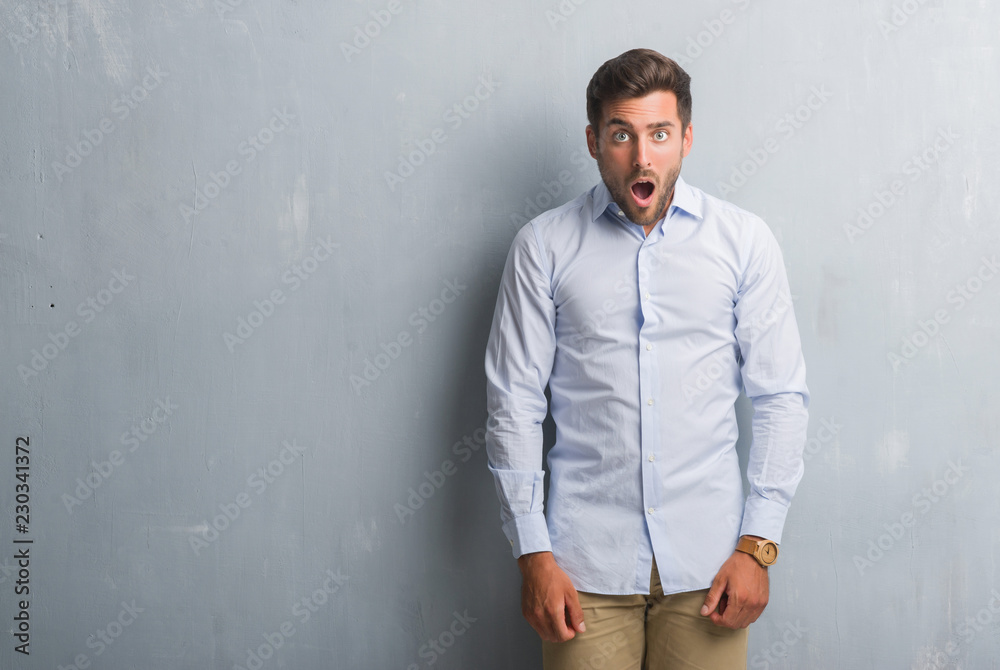 Handsome young business man over grey grunge wall wearing elegant shirt afraid and shocked with surprise expression, fear and excited face.