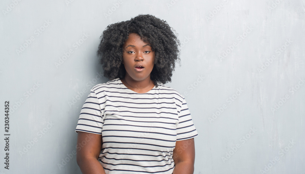 Young african american plus size woman over grey grunge wall afraid and shocked with surprise expression, fear and excited face. Young african american plus size woman over grey grunge wall afraid and shocked with surprise expression, fear and excited face.
