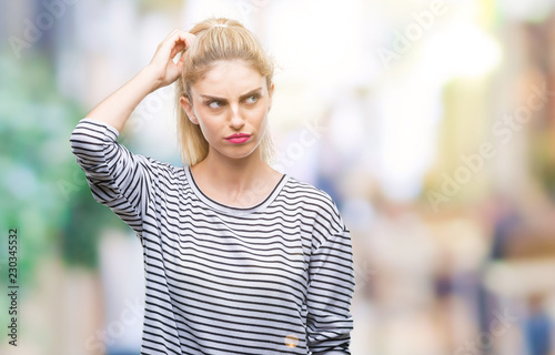 Young beautiful blonde woman wearing stripes sweater over isolated background confuse and wonder about question. Uncertain with doubt, thinking with hand on head. Pensive concept.