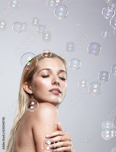 Beautiful young blonde woman with soap bubbles on grey background