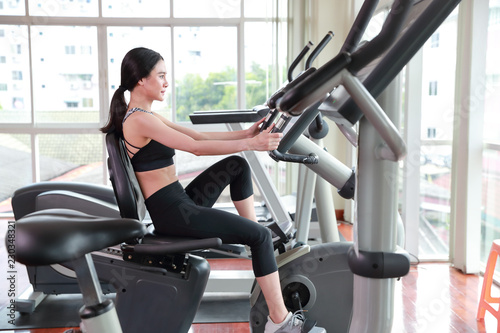portrait of young healthy and sporty woman bicycling on exercise machine in gym