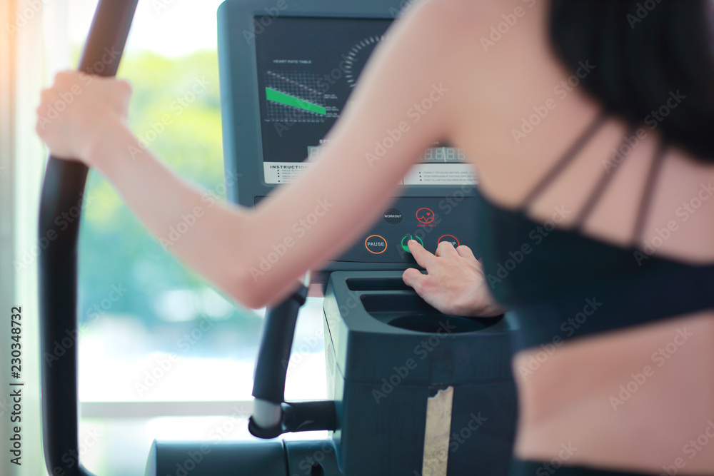 Naklejka premium portrait of young healthy and sporty woman using exercise machine in gym