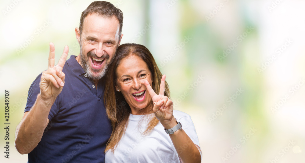 Middle age hispanic casual couple over isolated background smiling with happy face winking at the camera doing victory sign. Number two. Middle age hispanic casual couple over isolated background smiling with happy face winking at the camera doing victory sign. Number two.