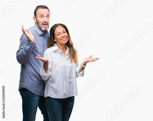 Middle age hispanic business couple over isolated background clueless and confused expression with arms and hands raised. Doubt concept.
