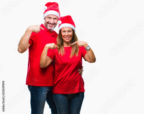 Middle age hispanic couple wearing christmas hat over isolated background looking confident with smile on face, pointing oneself with fingers proud and happy.