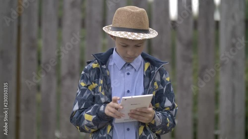farmer boy in a hat uses a tablet, stands against the fence photo