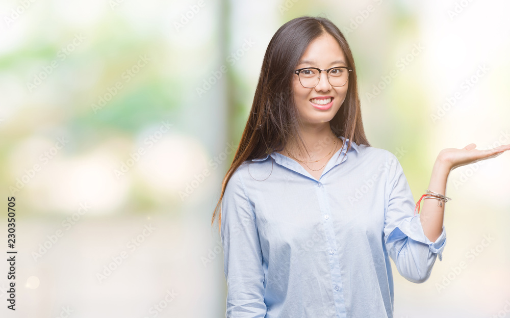 Young asian business woman wearing glasses over isolated background smiling cheerful presenting and pointing with palm of hand looking at the camera. Young asian business woman wearing glasses over isolated background smiling cheerful presenting and pointing with palm of hand looking at the camera.