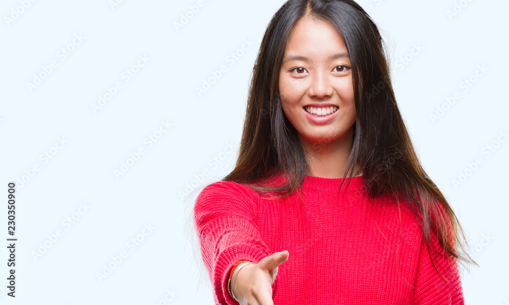 Young asian woman wearing winter sweater over isolated background smiling friendly offering handshake as greeting and welcoming. Successful business. Young asian woman wearing winter sweater over isolated background smiling friendly offering handshake as greeting and welcoming. Successful business.