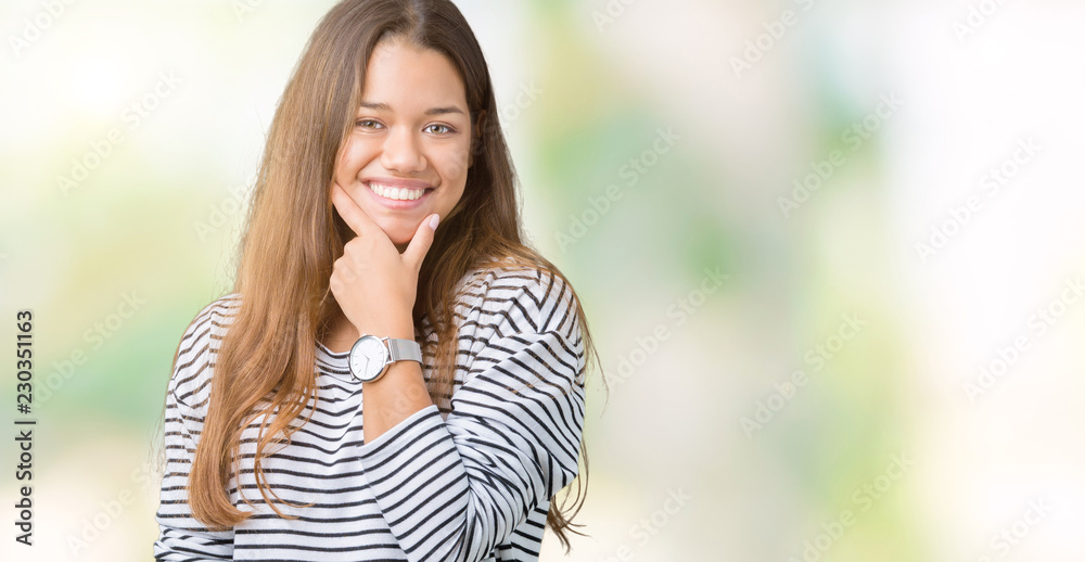 Young beautiful brunette woman wearing stripes sweater over isolated background looking confident at the camera with smile with crossed arms and hand raised on chin. Thinking positive. Young beautiful brunette woman wearing stripes sweater over isolated background looking confident at the camera with smile with crossed arms and hand raised on chin. Thinking positive.