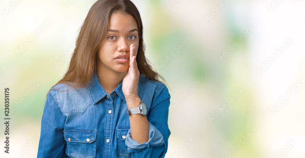 Young beautiful brunette woman wearing blue denim shirt over isolated background hand on mouth telling secret rumor, whispering malicious talk conversation Young beautiful brunette woman wearing blue denim shirt over isolated background hand on mouth telling secret rumor, whispering malicious talk conversation
