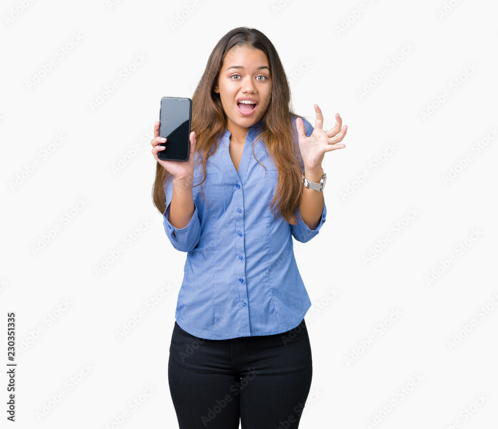 Young beautiful brunette business woman showing screen of smartphone over isolated background very happy and excited, winner expression celebrating victory screaming with big smile and raised hands Young beautiful brunette business woman showing screen of smartphone over isolated background very happy and excited, winner expression celebrating victory screaming with big smile and raised hands