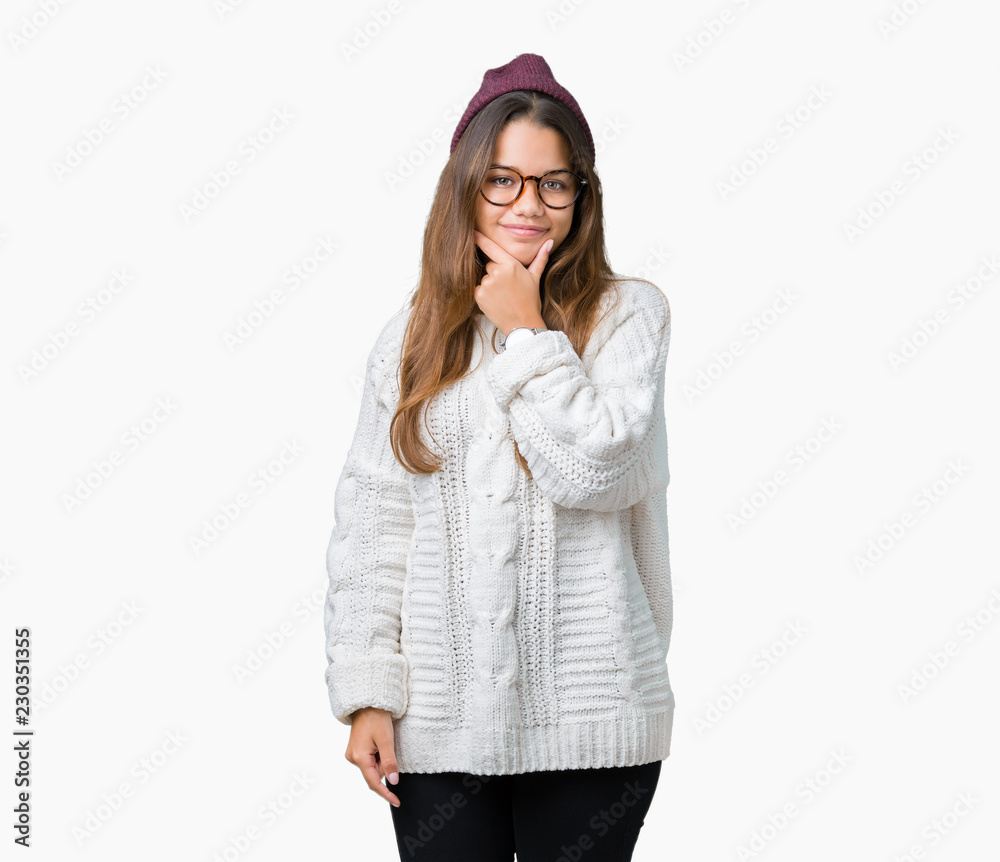 Young beautiful brunette hipster woman wearing glasses and winter hat over isolated background looking confident at the camera with smile with crossed arms and hand raised on chin. Thinking positive. Young beautiful brunette hipster woman wearing glasses and winter hat over isolated background looking confident at the camera with smile with crossed arms and hand raised on chin. Thinking positive.