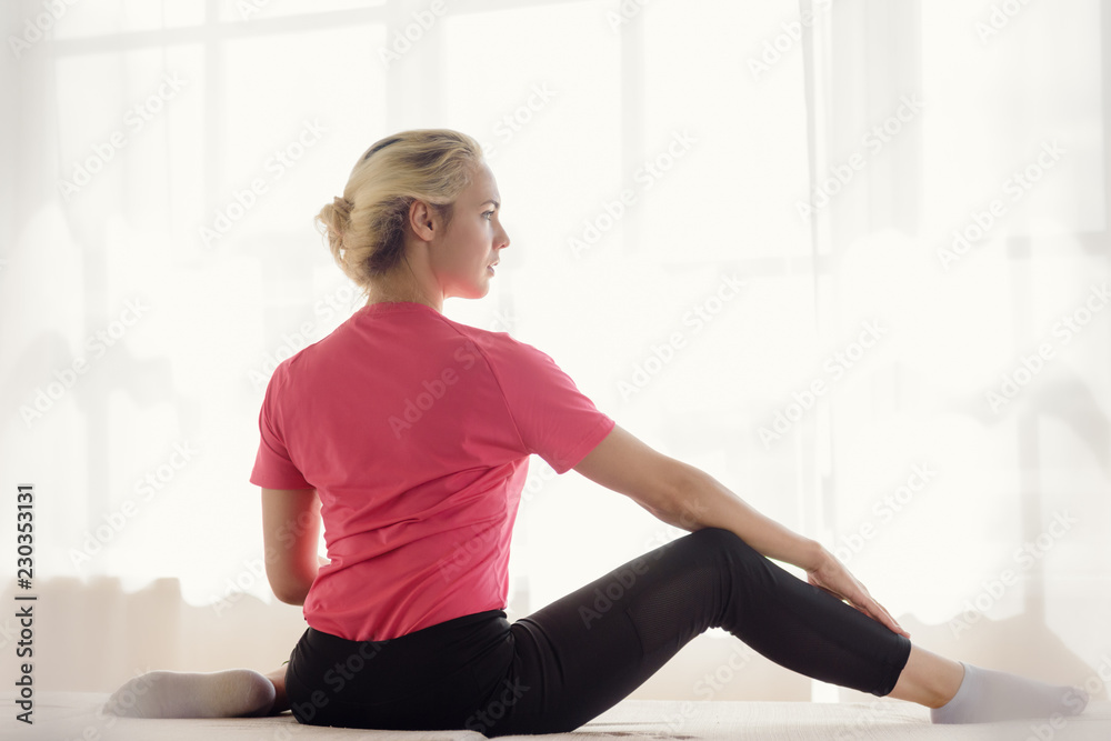 Fototapeta premium Back view of young woman doing fitness exercise at home
