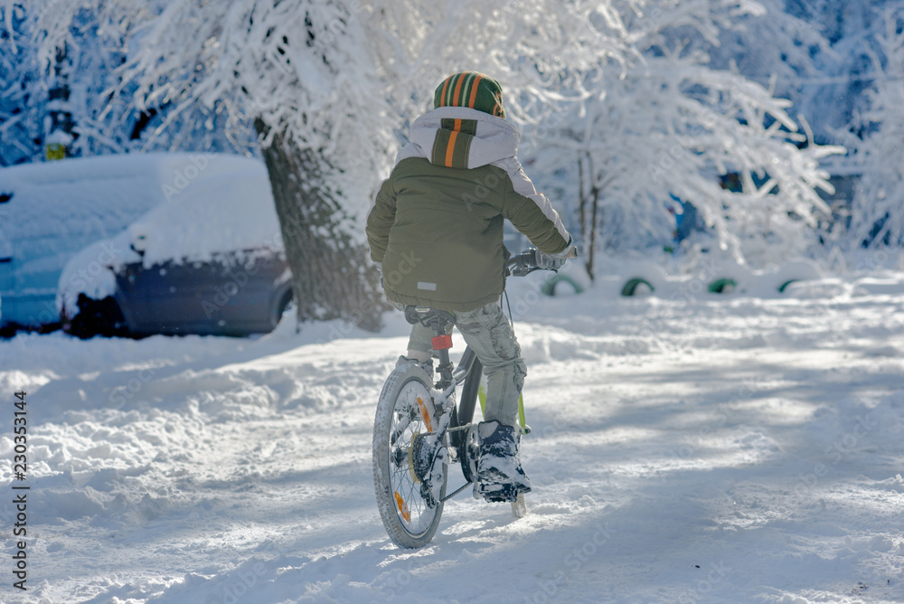 Back view of little boy riding bike in city on winter
