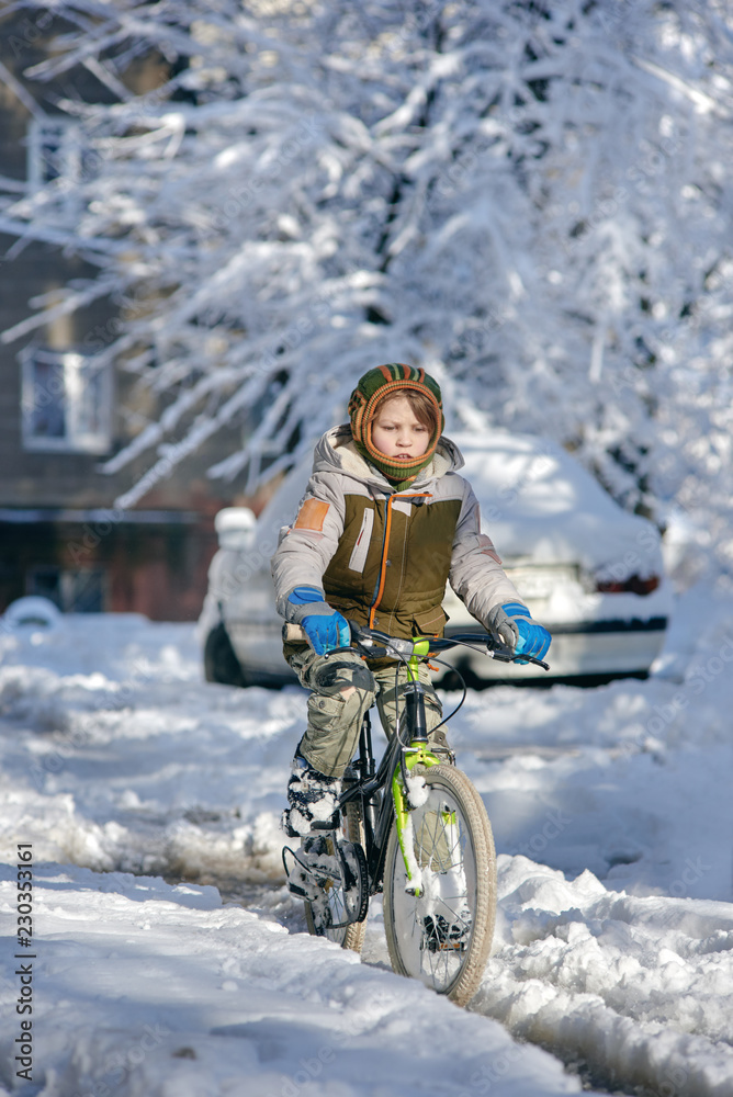 Boy riding bicycle in city on winter snowy day Boy riding bicycle in city on winter snowy day