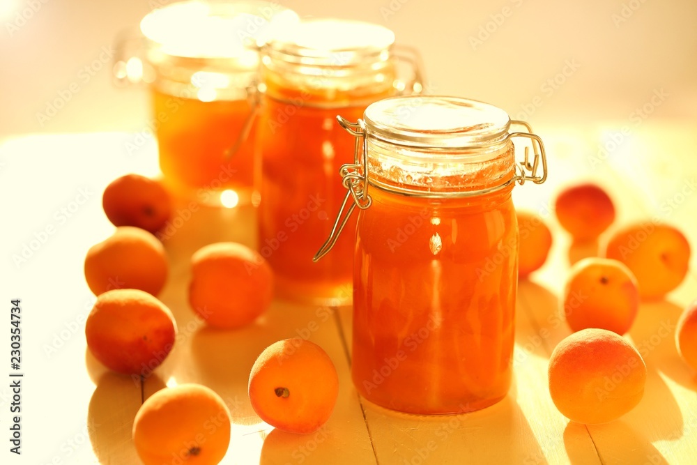 apricot jam set in glass jars and fresh ripe apricots on a yellow wooden board background in sun rays.Homemade jam apricot jam set in glass jars and fresh ripe apricots on a yellow wooden board background in sun rays.Homemade jam