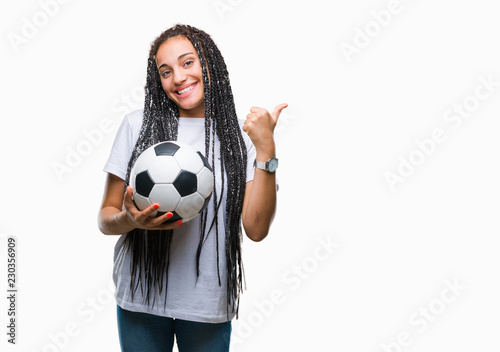 Young braided hair african american girl holding soccer ball over isolated background pointing and showing with thumb up to the side with happy face smiling