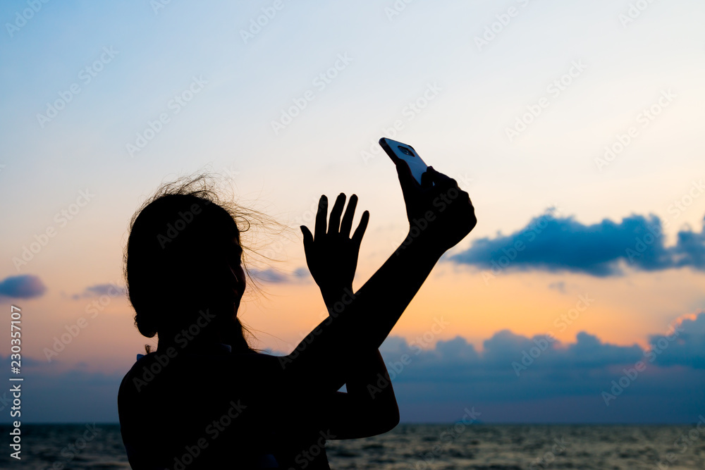 Silhouette picture of woman taking selfie during sunset
