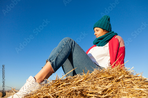 Fashion lifestyle portrait of young trendy woman dressed in pink coat, blue knitted hat  posing, laughing and smiling on haystick, autumn walking.  portrait of joyful woman photo