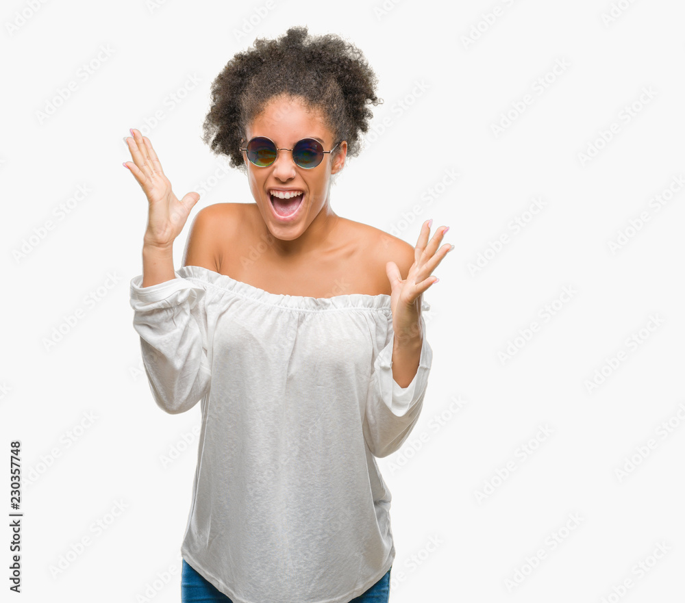 Young afro american woman wearing sunglasses over isolated background celebrating mad and crazy for success with arms raised and closed eyes screaming excited. Winner concept