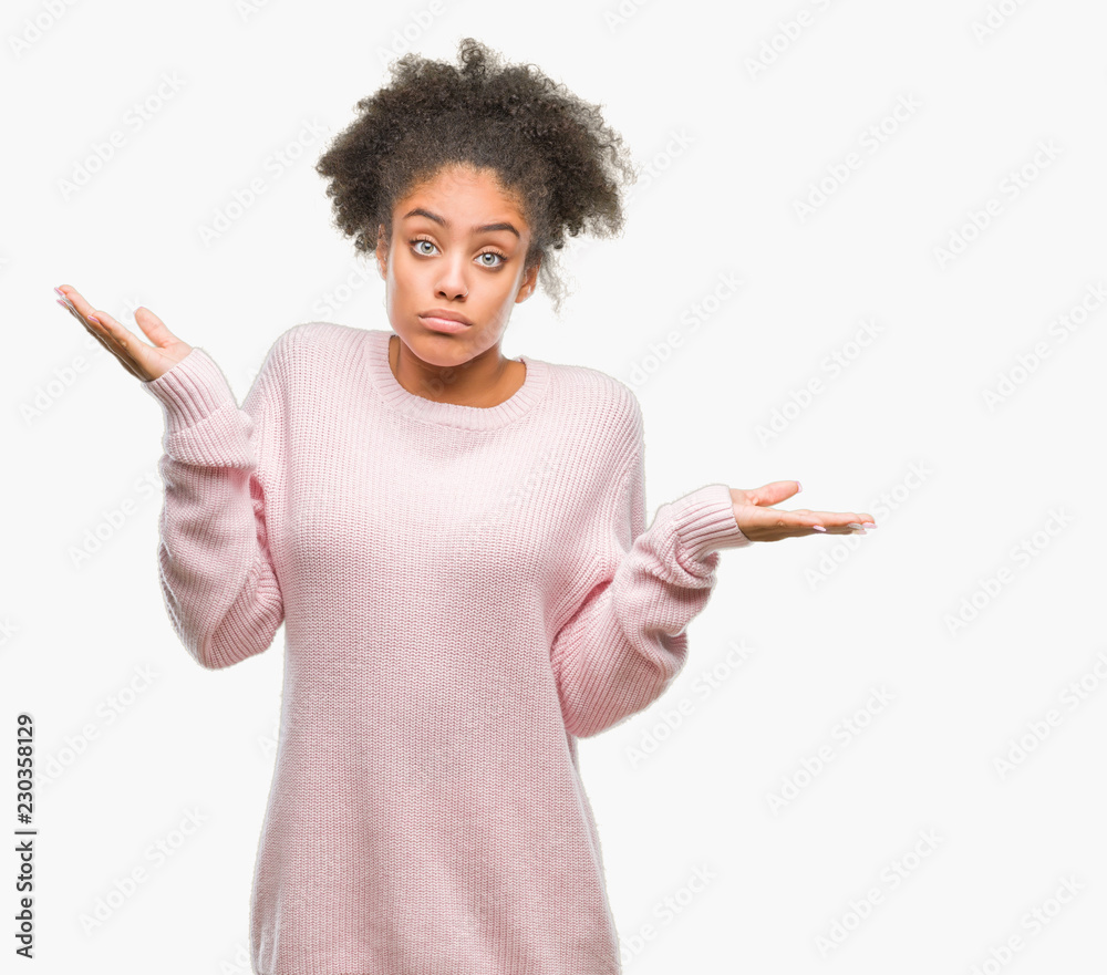 Young afro american woman wearing winter sweater over isolated background clueless and confused expression with arms and hands raised. Doubt concept. Young afro american woman wearing winter sweater over isolated background clueless and confused expression with arms and hands raised. Doubt concept.
