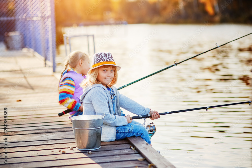 Little girls fishing on the lake, sitting on a wooden pontoon Little girls fishing on the lake, sitting on a wooden pontoon