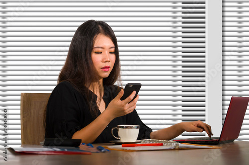 company corporate portrait of young beautiful and busy Asian Chinese woman working busy at modern office computer desk by venetian blinds window in business lifestyle © TheVisualsYouNeed