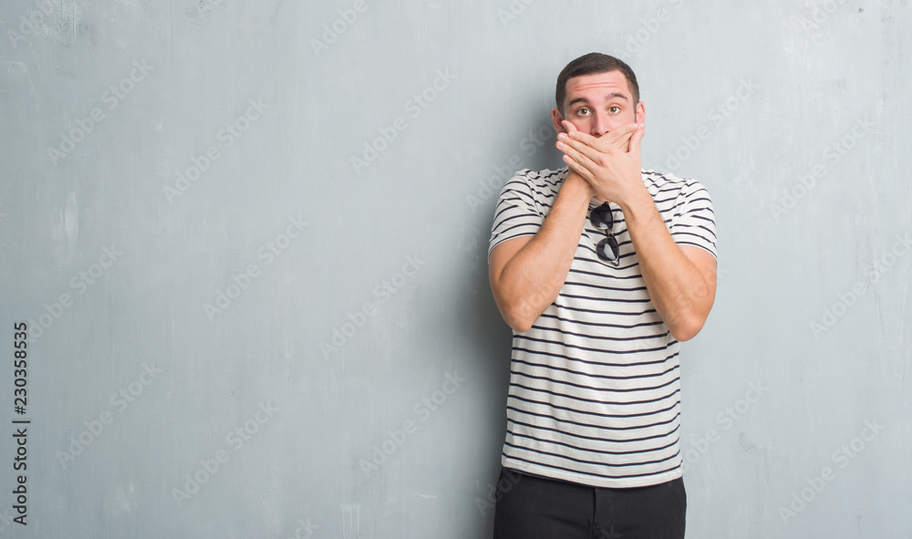 Young caucasian man over grey grunge wall shocked covering mouth with hands for mistake. Secret concept. Young caucasian man over grey grunge wall shocked covering mouth with hands for mistake. Secret concept.